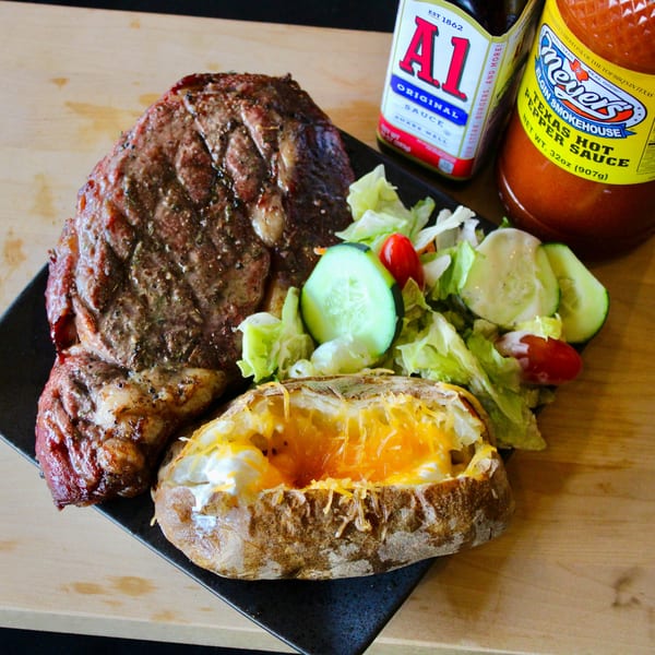 Meyer's Elgin Smokehouse steak with a loaded baked potato, side salad, and sauces.