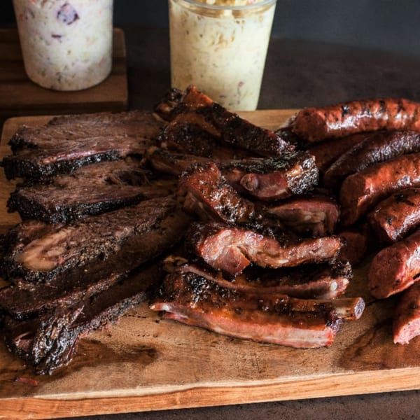 Meyer's Elgin Smokehouse BBQ platter with brisket, ribs, and sausage, with coleslaw in the background.