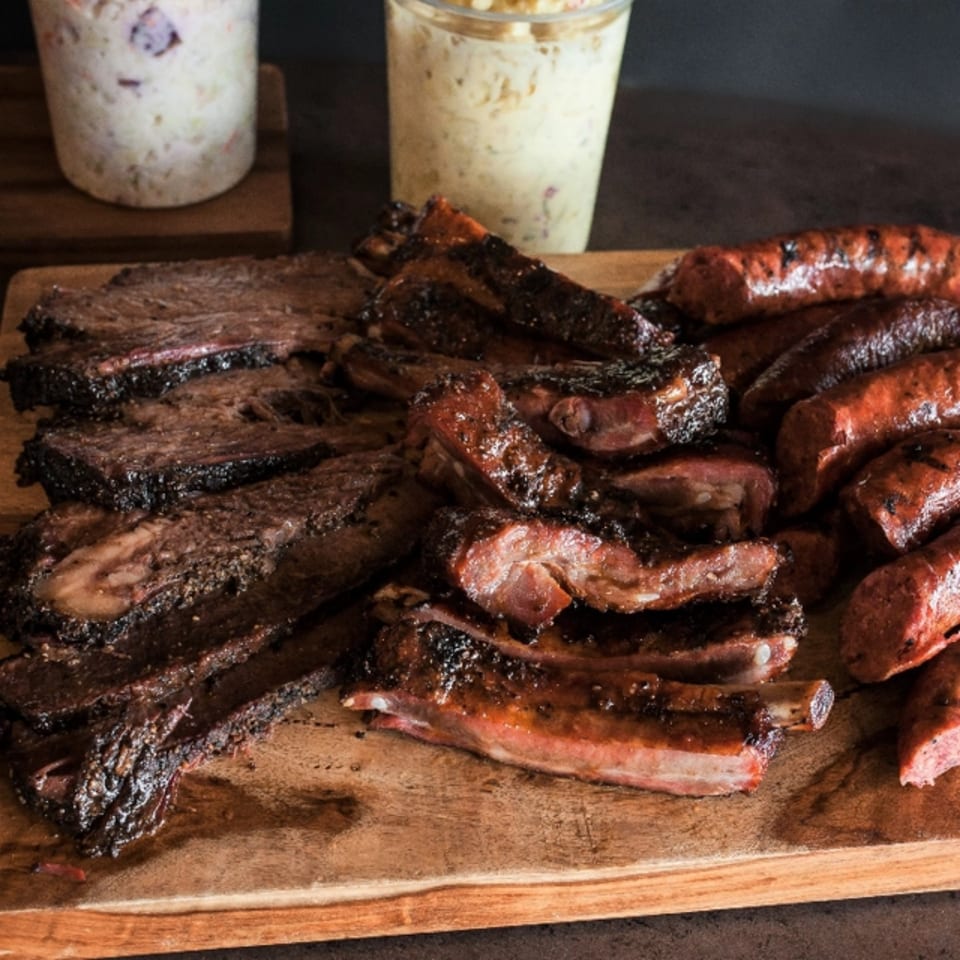 Meyer's Elgin Smokehouse BBQ platter with brisket, ribs, and sausage, with coleslaw in the background.