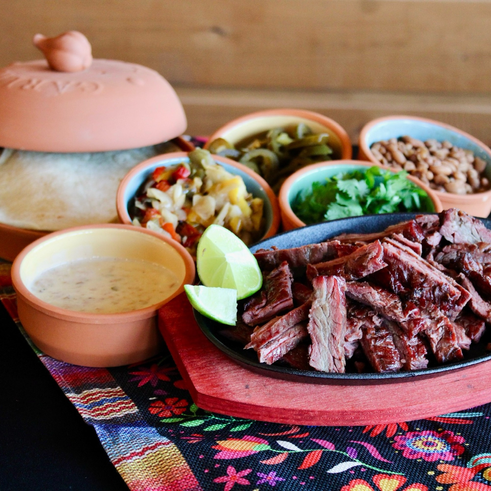 Meyer's Elgin Smokehouse sliced brisket with sides of beans, salsa, and tortillas.