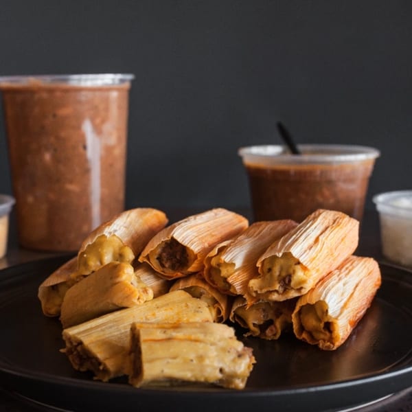 Meyer's Elgin Smokehouse tamales on a black plate with two cups of sauce in the background.
