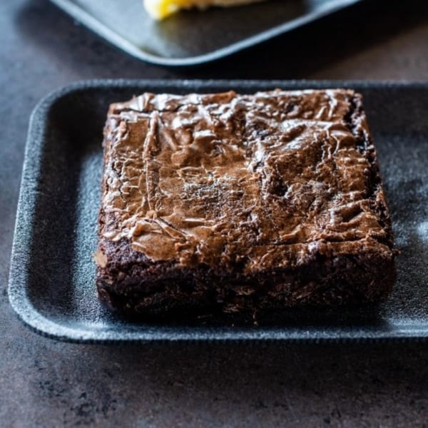 A rich, fudgy brownie with a crinkled top, served on a black tray.